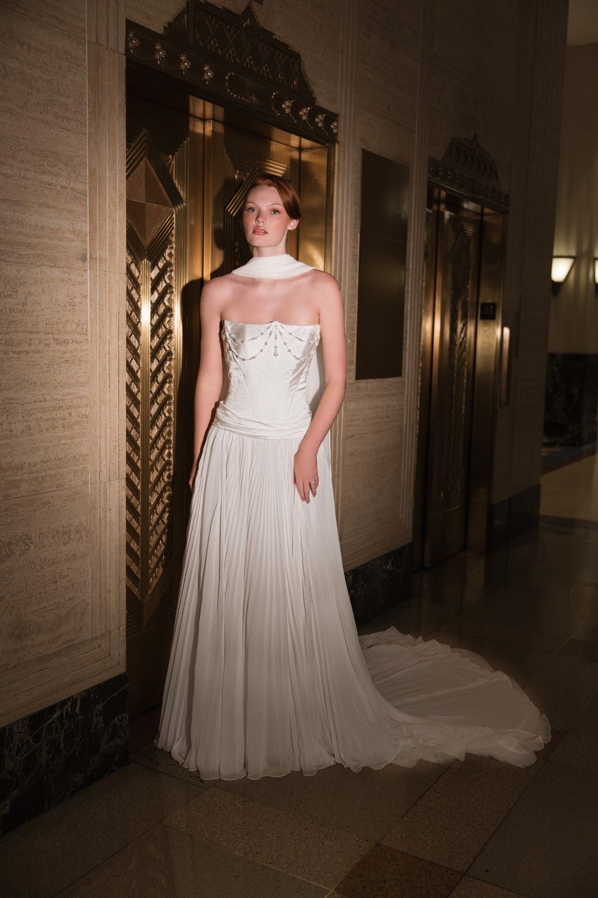 AURELLIA strapless beaded chain-draped satin and chiffon A-line wedding dress, front view in an Art Deco lobby, by Atelier Wu