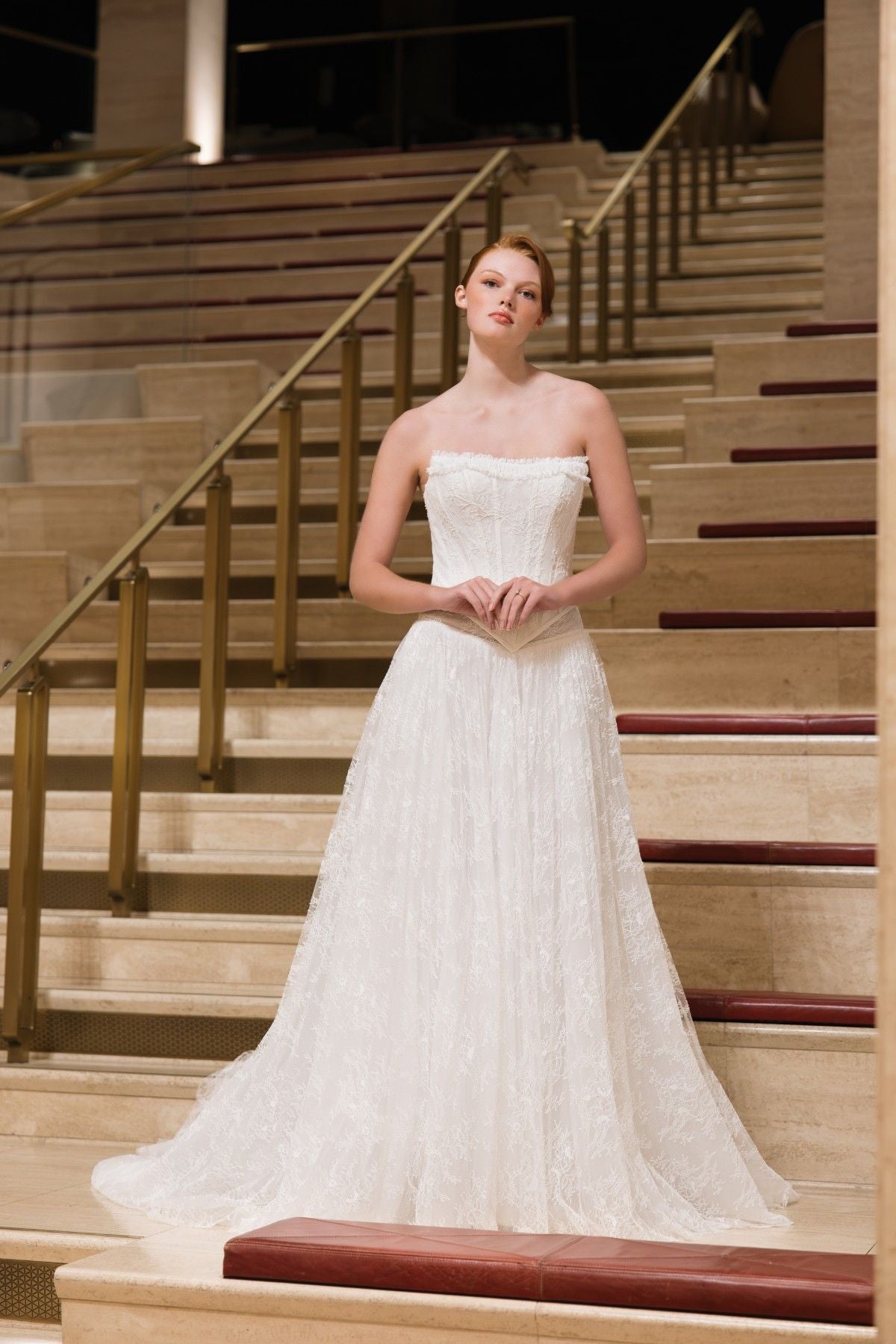 BLAKE strapless lace corset A-line wedding dress with ruffled trim and basque waist, full-length front view on a staircase, by Atelier Wu