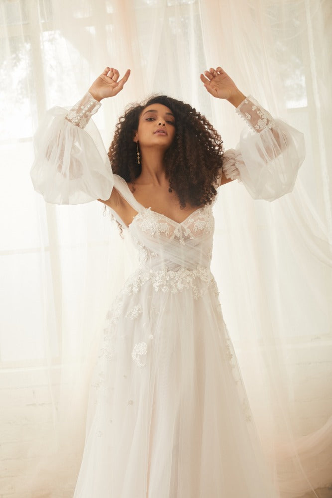 Mid shot of model wearing sky sleeves. Detachable sleeves made from soft tulle in a balloon shape. They sit on upper arm and have floral cuffs.'