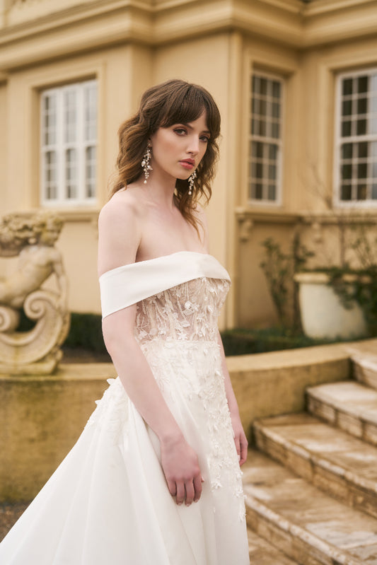 Model wears Theia dress with detachable overskirt in ivory satin with signature Jessica couture lace dripping from the waist. 