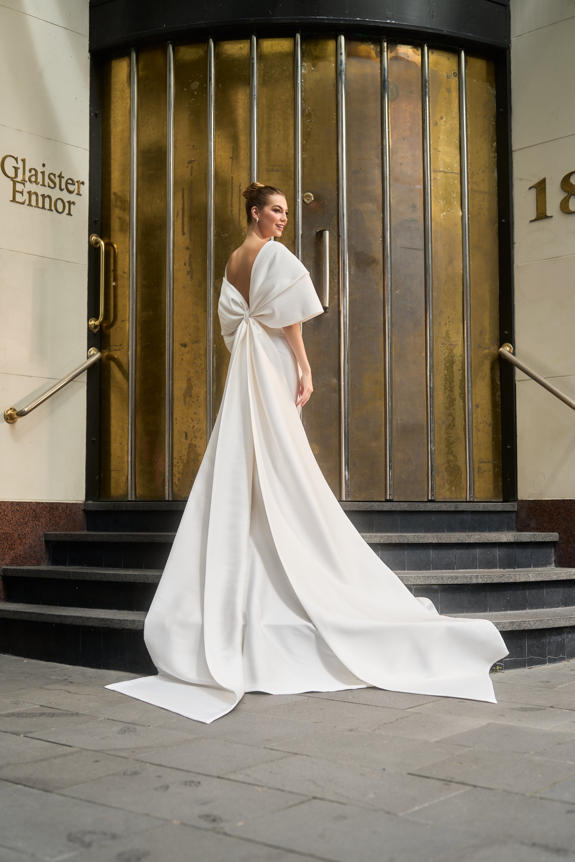 dramatic bow with train wraps around model's arms like shawl