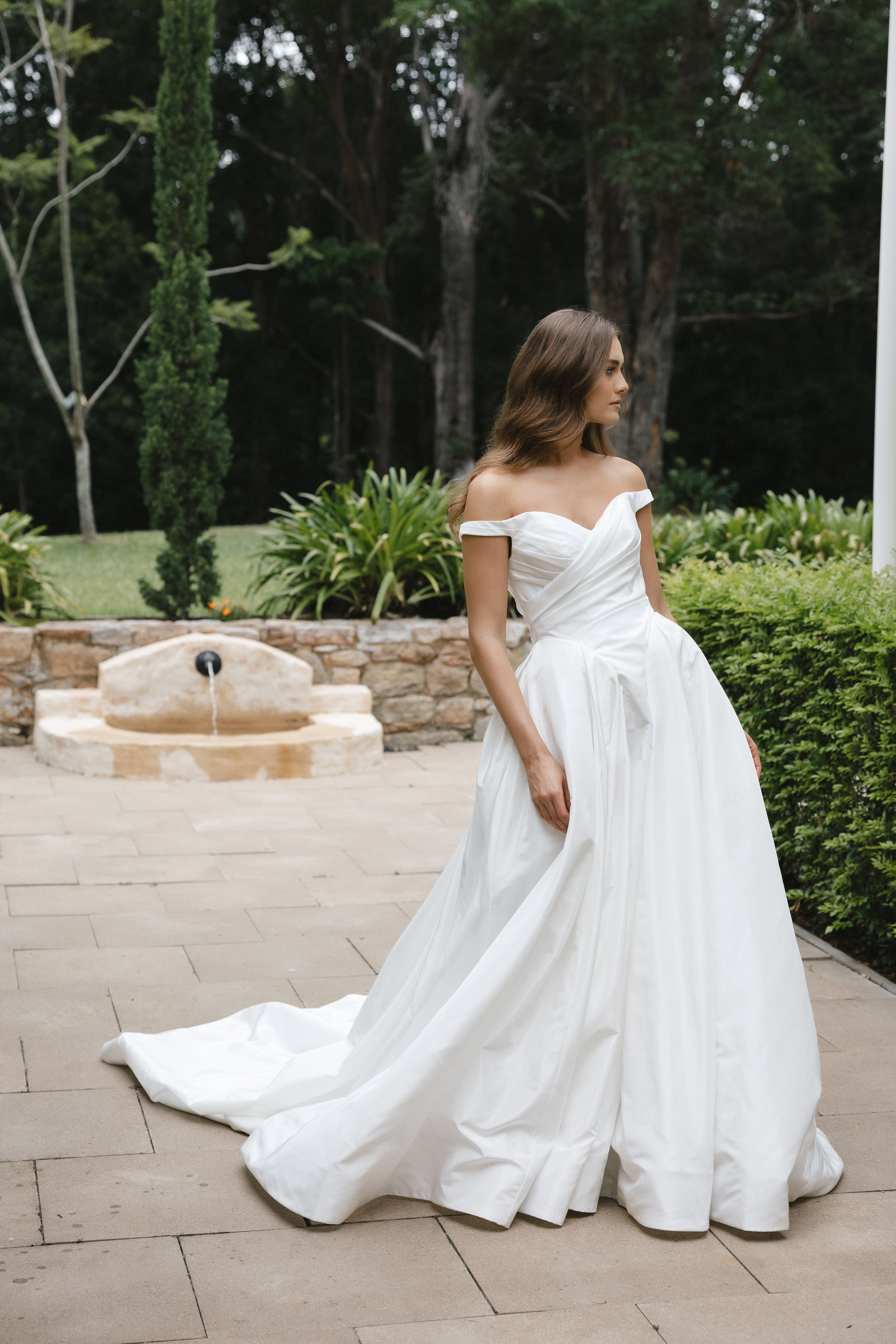Bridal gown Jodie features a clean A-line silhouette, off-shoulder sweetheart neckline, and basque waistline. Made from Taffeta, it’s designed for a timeless walk down the aisle by Roselle Collection Jessica Couture.