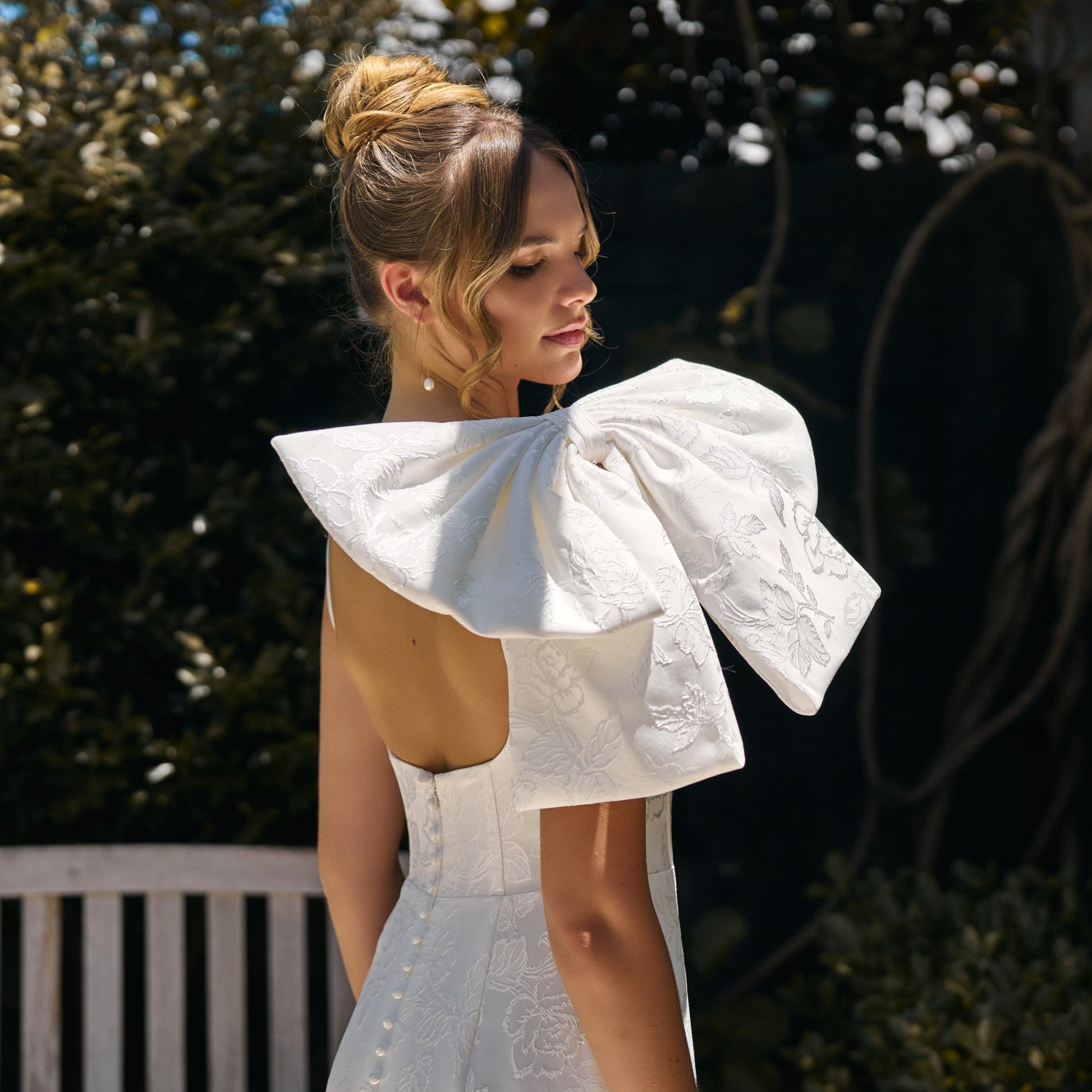 Large detachable bow in jacquard fabric sits on brides shoulder