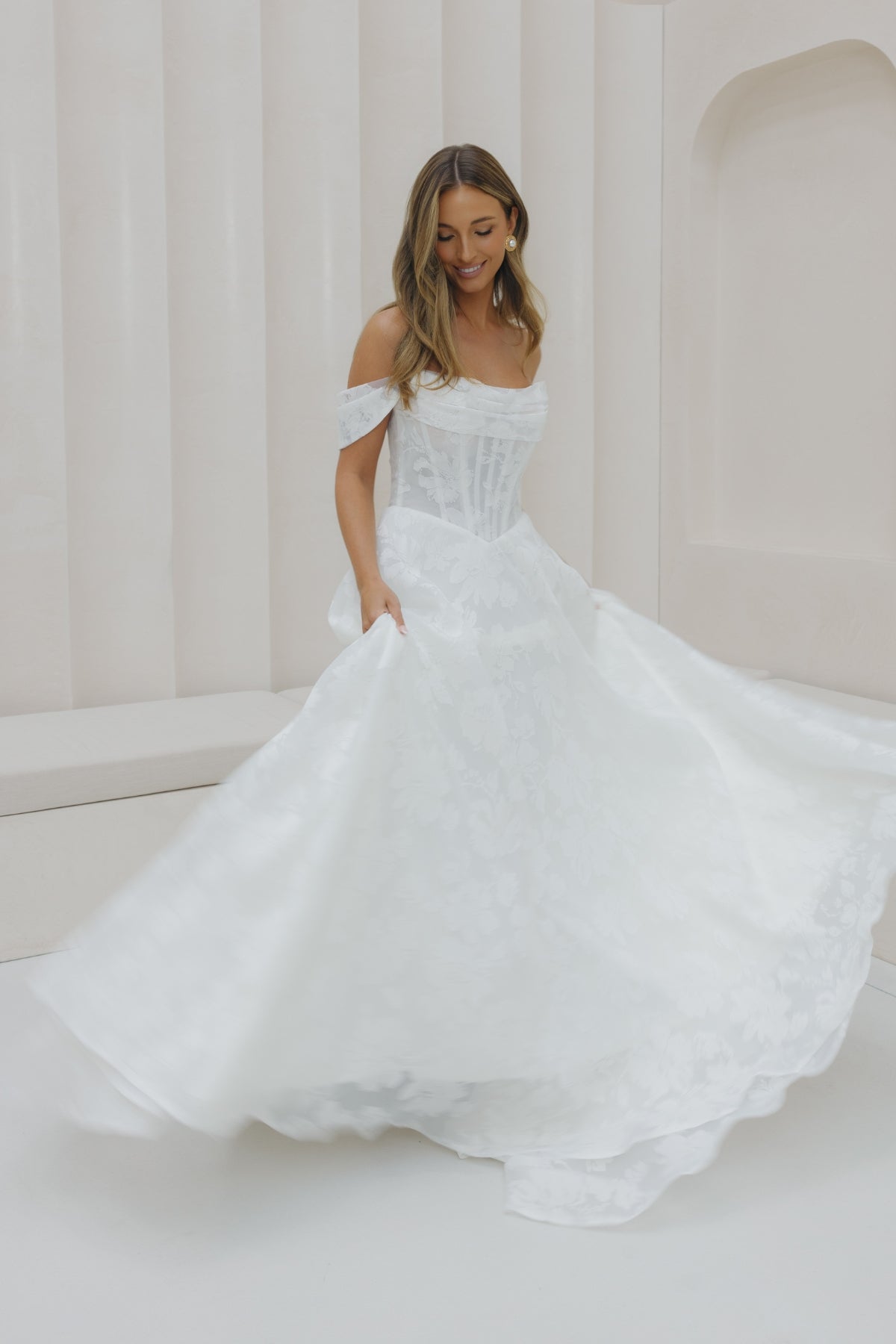 A-line wedding gown with off the shoulder neckline, ruched bust, and jacquard organza fabric. 