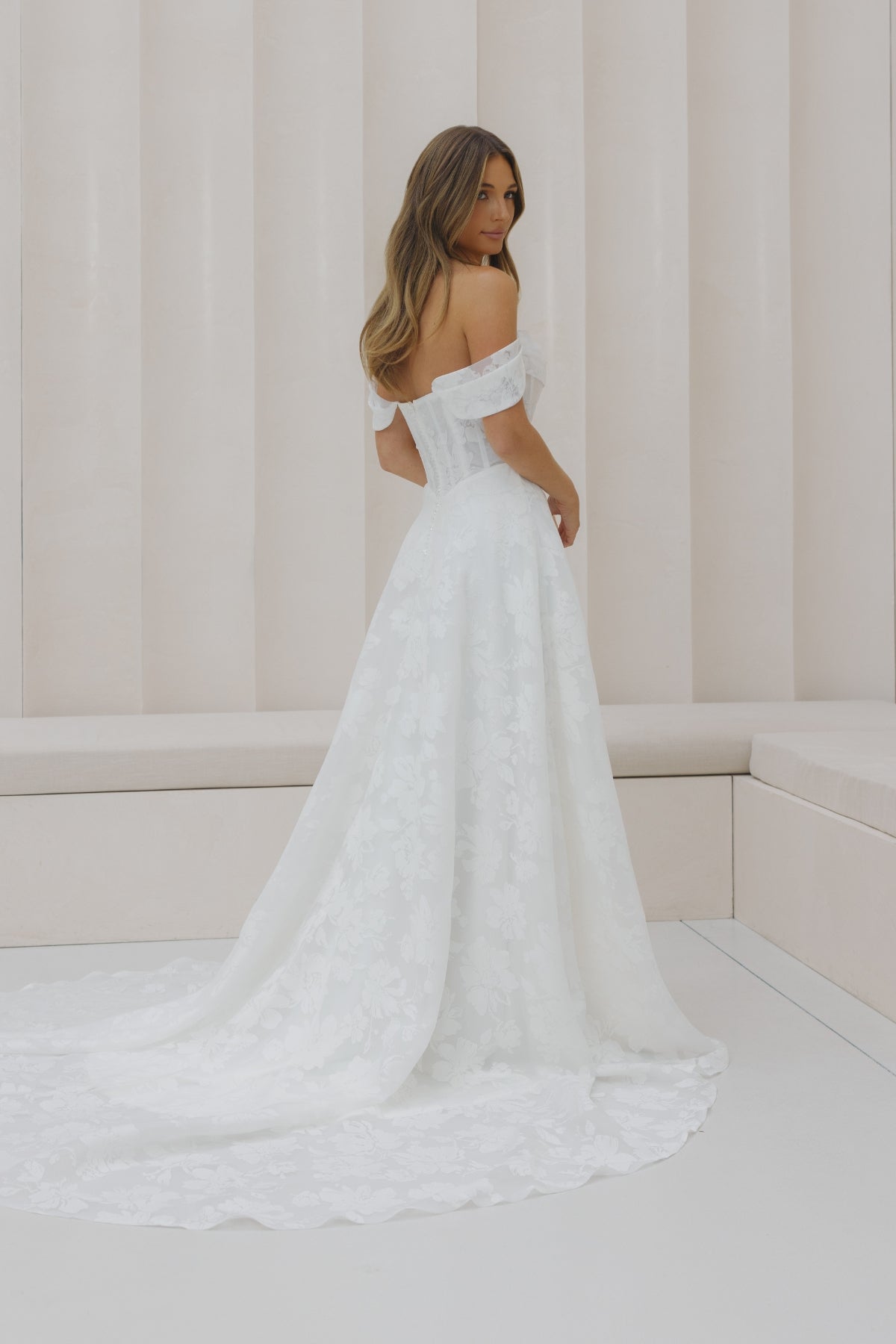 A-line wedding gown with off the shoulder neckline, ruched bust, and jacquard organza fabric. 