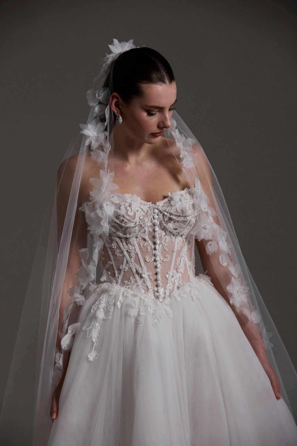 A-line Wedding dress featuring a tulle skirt, lace corseted bodice with basque waistline, cat-eye neckline, and buttons down the front of bodice. 