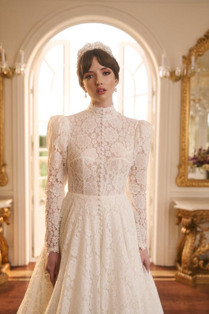 Close up of Tatyana gown in ivory lace with high neckline and mutton sleeves. Covered buttons run from neck to floor. Bodice is slightly sheer so as to see boning of corsetry underneath.