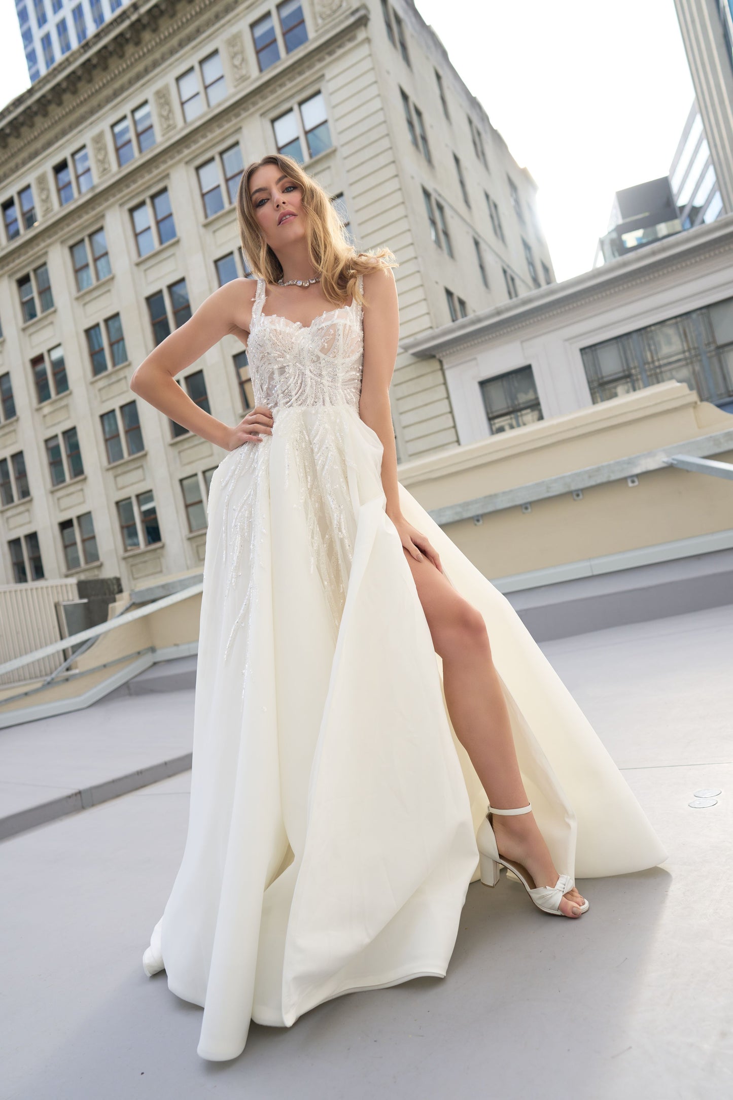 Raffael wedding dress from Jessica Coutures. Square neckline, low back A-line dress with organza fabric and glitter detailing at the bodice. Boning support, cinched waist, dramatic skirt. Hidden features include pockets and a split for easy movement.