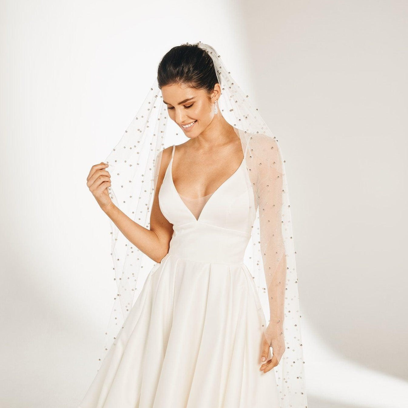 Bride stands against white backdrop in silver ball studded veil